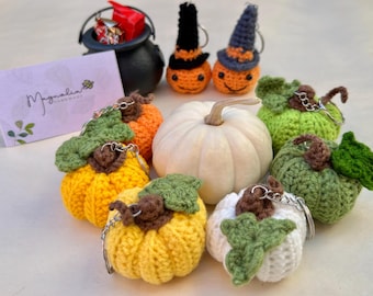 May include: A collection of crocheted pumpkin keychains in various colors, including orange, green, white, and yellow. The pumpkins have green leaves and are attached to silver key rings. There is also a white pumpkin with a brown stem and a small white pumpkin with a green leaf.