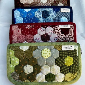 May include: Four rectangular zippered pouches featuring a quilted hexagon patchwork design. Each pouch displays a unique color palette of green, red, blue, or brown tones with various fabric patterns and a small white label reading Magnolia Handmade.
