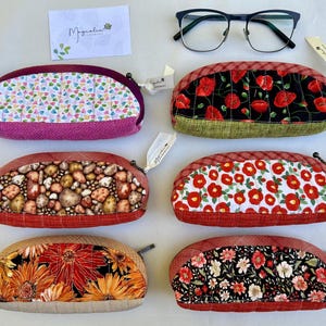 K&ouml;nnte beinhalten: Sechs halbkreisf&ouml;rmige, gesteppte Etuis mit Rei&szlig;verschl&uuml;ssen, nummeriert von 7 bis 12. Die Designs umfassen bunte Herzen, rote Mohnblumen auf Schwarz, braune Steine, rote Blumen auf Wei&szlig;, orangefarbene Sonnenblumen und kleine Blumenmuster.