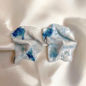 Può includere: Un paio di orecchini in ceramica blu e bianca con un design testurizzato e astratto.