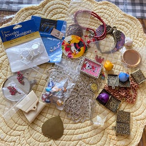 May include: Assortment of jewelry making supplies including beads, charms, chains, and findings.  The supplies are in clear plastic bags on a yellow and white patterned surface.  The bags are labeled "Jewelry Designer" and "Ultimate Crystals".