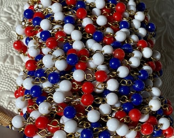Puede incluir: Una hebra de 15 metros de cuentas de 6 mm de diámetro en rojo, blanco y azul. Las cuentas están enhebradas en una cadena dorada.