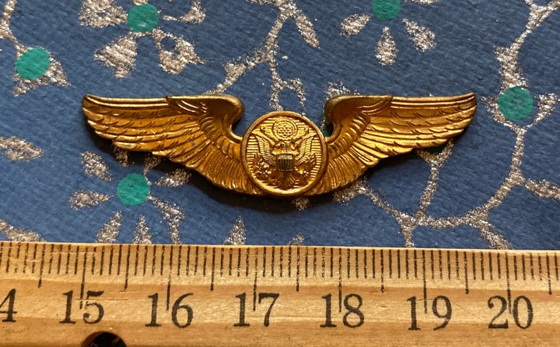 Puede incluir: Unas alas de piloto militar doradas con un emblema redondo dorado en el centro. El emblema presenta un &aacute;guila calva con un escudo en el pecho. Las alas miden aproximadamente 4,4 cm de ancho.