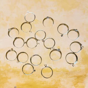 以下が含まれることがあります： 片側に小さなループが付いた銀色の金属製の輪の集まり。輪は薄い茶色の表面に円形に配置されています。