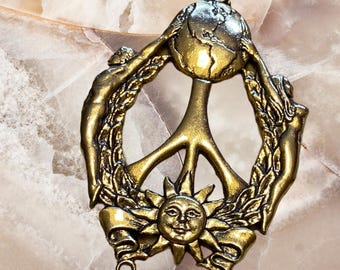 Puede incluir: Encanto de metal dorado en forma de signo de paz con un globo terráqueo, un sol y dos figuras sosteniendo el globo. El encanto tiene dos anillos de salto para sujetarlo a un collar o pulsera.