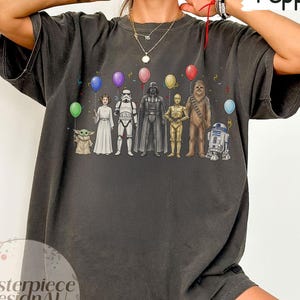 May include: Dark grey t-shirt with a Star Wars character design holding balloons. The characters include Yoda, Princess Leia, a Stormtrooper, Darth Vader, C-3PO, Chewbacca, and R2-D2. The text "Pepper" is in the upper right corner.