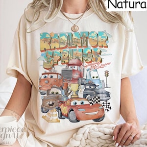 May include: A cream colored t-shirt with a graphic print of the Cars characters from the movie Cars. The graphic includes the text "Radiator Springs" and "Lightning McQueen".