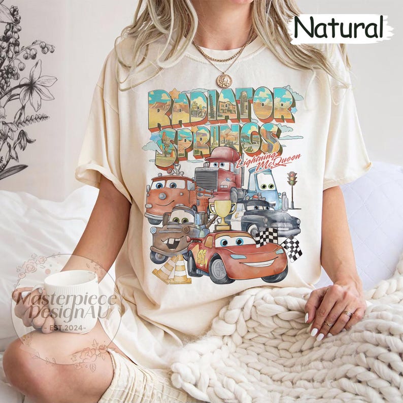 May include: A cream colored t-shirt with a graphic print of the Cars characters from the movie Cars. The graphic includes the text "Radiator Springs" and "Lightning McQueen".