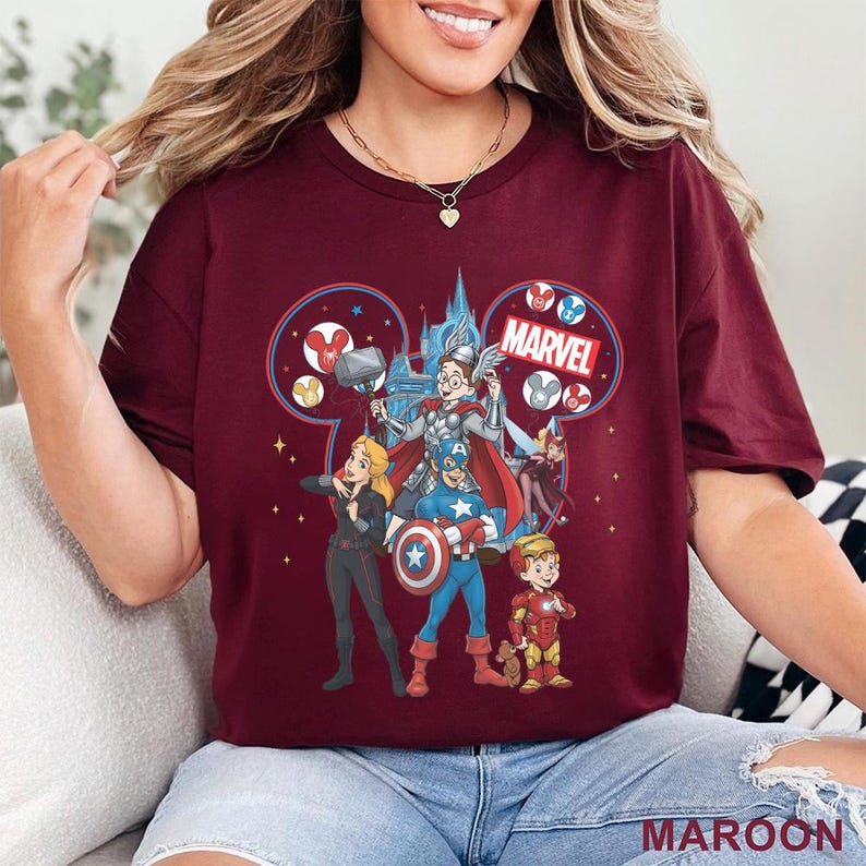 Może przedstawiać: Bordowa koszulka z motywem Marvel inspirowanym Disneyem. Grafika przedstawia postacie Marvela, takie jak Kapitan Ameryka, Thor i Iron Man, na tle zamku. Słowo "MARVEL" jest wyraźnie widoczne.