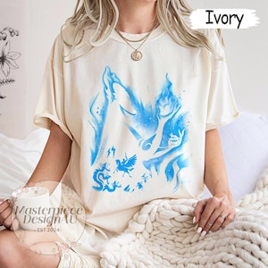 May include: Ivory t-shirt with a blue graphic depicting mythical figures and flames. The shirt has short sleeves and a loose fit. The text "Masterpiece DesignAU - EST.2024-" is visible on a white mug.