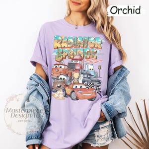 May include: A purple t-shirt with a graphic of the Cars characters from the movie Cars. The graphic includes the text "Radiator Springs" and "Lightning McQueen".