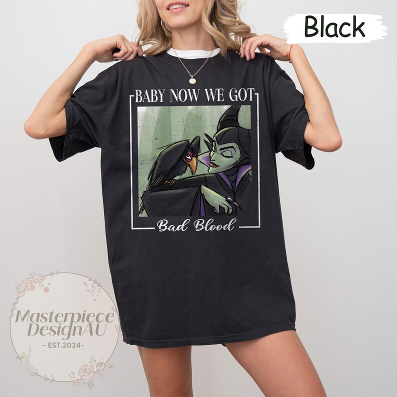 May include: Black t-shirt featuring a graphic of a raven and a villainous character with the text "BABY NOW WE GOT" and "BAD BLOOD". The design is framed in a white rectangle. The shirt is a comfortable, casual style.