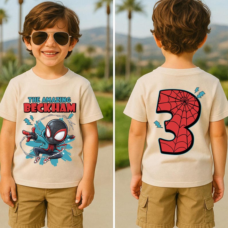 May include: Beige t-shirt with a superhero graphic and the text "THE AMAZING BECKHAM" on the front. The back of the shirt features a large red number "3" with a spiderweb design. The shirt is paired with khaki shorts.