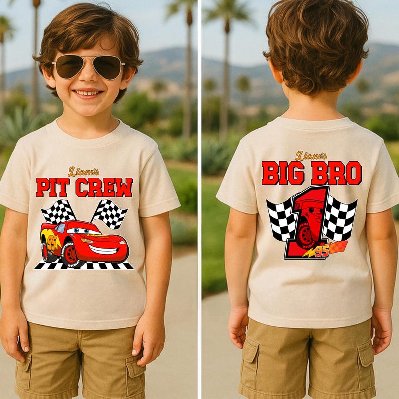 May include: A tan t-shirt featuring a red race car graphic with the text "Liam's PIT CREW". The back of the shirt says "Liam's BIG BRO" in red letters with a race car graphic and checkered flags. The shirt is worn by a child.