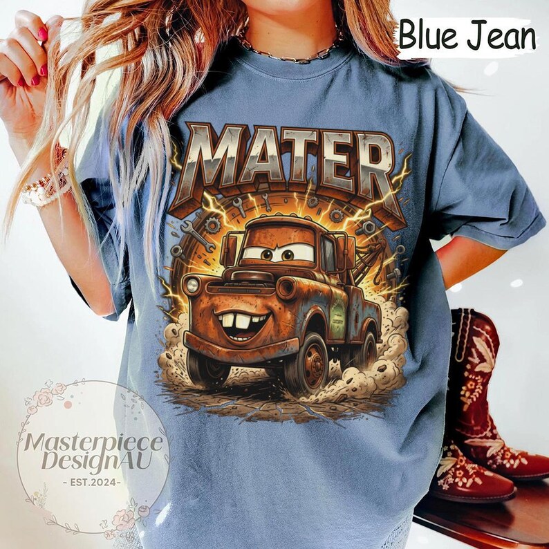 May include: Blue jean colored t-shirt featuring a cartoon image of Mater from the movie Cars. The graphic includes the name "MATER" in large, distressed lettering above the character. The shirt has a relaxed fit.