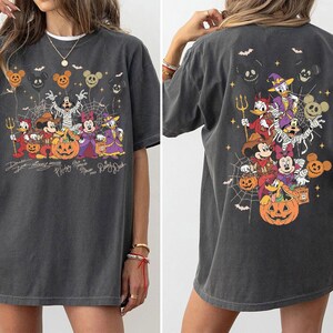 May include: A charcoal gray t-shirt featuring a Halloween-themed graphic of Disney characters including Mickey Mouse, Minnie Mouse, Donald Duck, Daisy Duck, Goofy, and Pluto. The design includes pumpkins, spiderwebs, and bats with character names.
