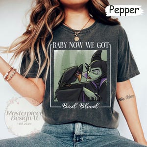 May include: Dark grey t-shirt featuring a graphic of Maleficent and a raven with the text "BABY NOW WE GOT" above and "Bad Blood" below. The shirt has a vintage, worn look.