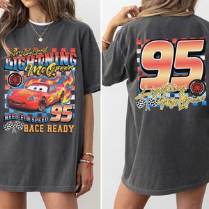 Puede incluir: Camiseta gris oscuro con Lightning McQueen de la pel&iacute;cula Cars. El gr&aacute;fico frontal incluye el coche, llamas y texto. La parte trasera muestra un gran "95" y el nombre del personaje. La camiseta tiene un aspecto vintage y desgastado.
