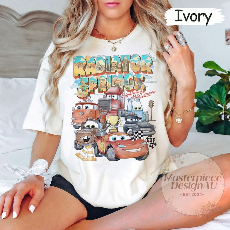 May include: White t-shirt with a graphic of the Cars characters from the movie Cars. The graphic includes the text "Radiator Springs" and "Lightning McQueen".
