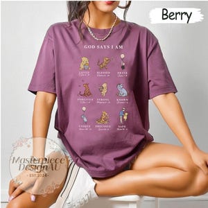 K&ouml;nnte beinhalten: Ein lila T-Shirt mit einem Winnie Puuh-Design. Das Shirt zeigt den Text "Gott sagt, ich bin" und ein Raster mit Winnie Puuh-Charakteren mit Bibelversen.