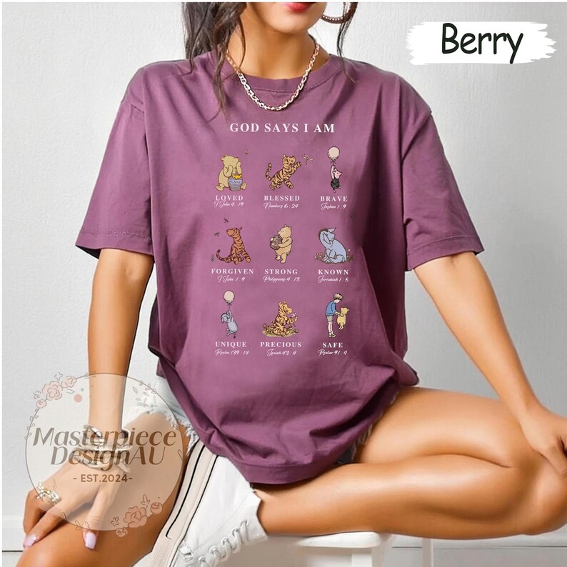 K&ouml;nnte beinhalten: Ein lila T-Shirt mit einem Winnie Puuh-Design. Das Shirt zeigt den Text "Gott sagt, ich bin" und ein Raster mit Winnie Puuh-Charakteren mit Bibelversen.