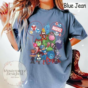 Może przedstawiać: Niebieska koszulka dżinsowa z kolorową grafiką postaci Disneya i Marvela. Projekt zawiera napis "Marvel" i słowa "Blue Jean". Koszulka ma luźny kr&oacute;j.