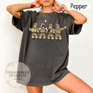 Peut inclure: T-shirt gris fonc&eacute; avec un dessin anim&eacute; de quatre explorateurs en tenues kaki, chapeaux et bottes. L'un tient une carte, un autre des jumelles, un troisi&egrave;me un appareil photo et le dernier pointe. Le mot "Pepper" est &eacute;crit en haut &agrave; droite.
