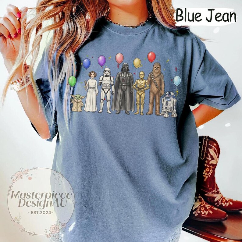 May include: Blue jean coloured t-shirt featuring a Star Wars character graphic with balloons. The graphic includes characters like Darth Vader, Chewbacca, and R2-D2. The shirt has the text "Blue Jean" at the top.