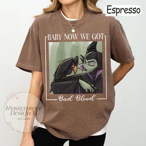 May include: Espresso-colored t-shirt featuring a graphic of a raven and a villainous character with the text "BABY NOW WE GOT BAD BLOOD". The shirt is a relaxed fit.