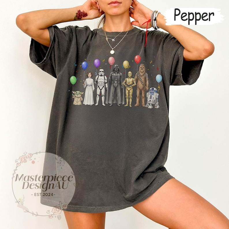 May include: Dark grey t-shirt with a Star Wars character design holding balloons. The characters include Yoda, Princess Leia, a Stormtrooper, Darth Vader, C-3PO, Chewbacca, and R2-D2. The text "Pepper" is in the upper right corner.
