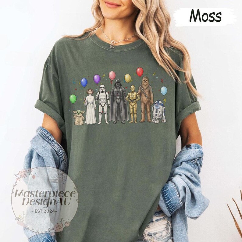 May include: Moss green t-shirt with a Star Wars character design. The graphic shows characters such as Darth Vader and R2-D2, each with a balloon. The shirt also has the text "Masterpiece Design AU - EST. 2024".
