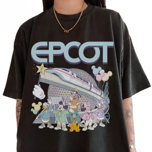 May include: Black t-shirt featuring the word "EPCOT" in light blue, with a graphic of a monorail, Spaceship Earth, and Disney characters. The characters include Mickey Mouse, Minnie Mouse, Donald Duck, Goofy, and Daisy Duck.