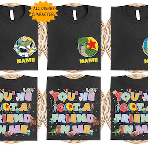 May include: Black t-shirts featuring Toy Story characters. Some shirts show Buzz Lightyear, Rex, or Woody with the text NAME. Others display the text YOU'VE GOT A FRIEND IN ME surrounded by various Toy Story character illustrations and stars.