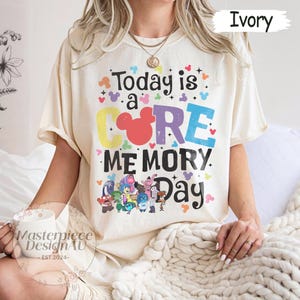May include: Ivory-colored t-shirt with the text "Today is a CORE MEMORY Day" in colorful letters. The design includes cartoon characters and Mickey Mouse ears. The shirt is a relaxed fit.