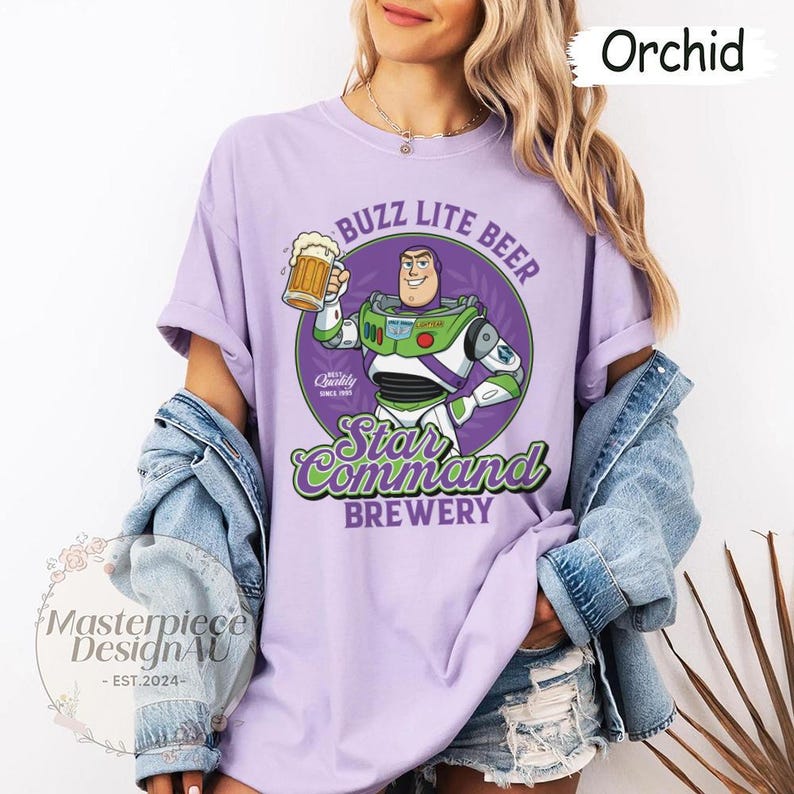 May include: Orchid-colored t-shirt featuring a graphic of Buzz Lightyear holding a beer mug, with the text "Buzz Lite Beer" and "Star Command Brewery". The shirt also has the text "Masterpiece DesignAU - EST.2024-".