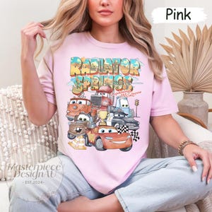 May include: Pink t-shirt with a graphic of the Cars characters from the movie Cars. The graphic includes the text "Radiator Springs" and "Lightning McQueen".