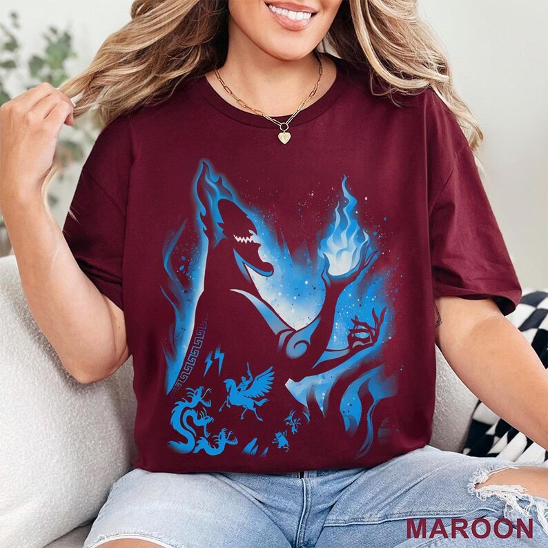 May include: Maroon t-shirt with a blue silhouette of a character with blue flames and other blue graphics. The word "MAROON" is printed in white at the bottom. The shirt has short sleeves and a crew neck.