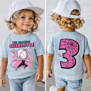 Pu&ograve; includere: T-shirt azzurra con grafica di supereroe e la scritta "THE AMAZING CHARLOTTE" sul davanti. Il retro della maglietta mostra un numero 3 rosa con un disegno a ragnatela e fulmini.