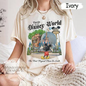 May include: Ivory-colored t-shirt featuring a colorful graphic of Disney World with Mickey Mouse. The text "Florida Disney World" and "The Most Magical Place On Earth" are also displayed. The shirt is a relaxed fit.