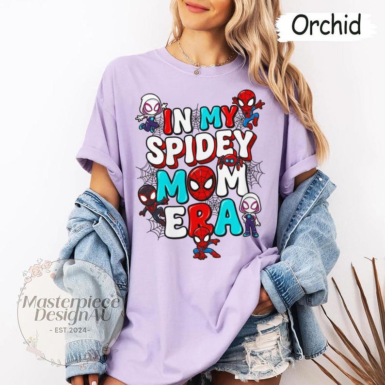 Puede incluir: Camiseta color orqu&iacute;dea con el texto "IN MY SPIDEY MOM ERA" en rojo, blanco y turquesa. Personajes de Spider-Man y telara&ntilde;as rodean el texto. La camiseta es de estilo casual.