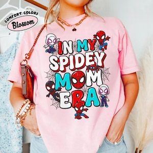Puede incluir: Camiseta rosa con el texto "IN MY SPIDEY MOM ERA" en rojo, blanco y azul. La camiseta presenta personajes de dibujos animados de Spider-Man y telara&ntilde;as. La camiseta tambi&eacute;n tiene las palabras "Comfort Colors Blossom" en un c&iacute;rculo.