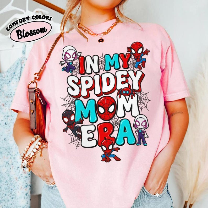 Puede incluir: Camiseta rosa con el texto "IN MY SPIDEY MOM ERA" en rojo, blanco y azul. La camiseta presenta personajes de dibujos animados de Spider-Man y telara&ntilde;as. La camiseta tambi&eacute;n tiene las palabras "Comfort Colors Blossom" en un c&iacute;rculo.