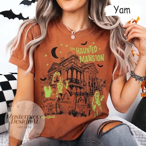 May include: A burnt orange t-shirt featuring a graphic of a haunted mansion with the text "The Haunted Mansion". The design includes bats, a crescent moon, and tombstones. The shirt also has the text "Master Gracey Laid to Rest" and "Dear Departed Brother Dave".