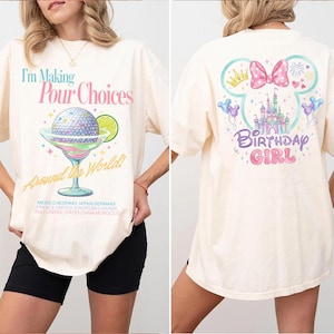 May include: Cream-colored t-shirt with the text "I'm Making Pour Choices Around the World!" and a cocktail graphic on the front. The back features a Disney-themed design with a castle, bow, and the words "Birthday Girl".
