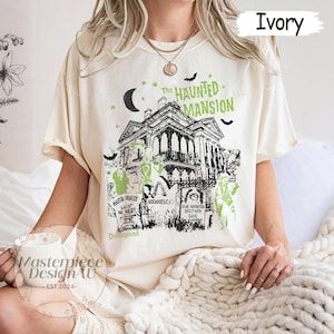 May include: Ivory-colored t-shirt featuring a graphic of The Haunted Mansion, with a spooky house design, moon, stars, and bats. The text "The Haunted Mansion" is above the house, and "Disneyland" is below. The shirt also has the text "Master Gracey Laid to Rest" and "Dear Departed Brother Dave".