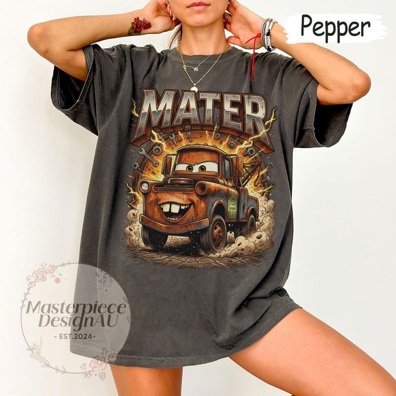 May include: Pepper-colored t-shirt featuring a graphic of Mater from the Cars movie. The design includes the word "MATER" above the character, with lightning bolts and tools surrounding the image. The shirt has a relaxed fit.