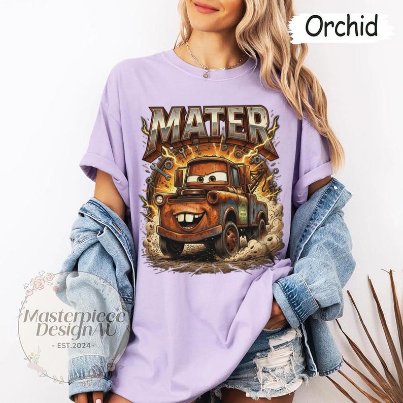May include: Orchid-colored t-shirt featuring a graphic of Mater from the Cars movie. The design includes the word "MATER" in a metallic font, with a cartoon image of Mater. The shirt is part of a clothing collection.