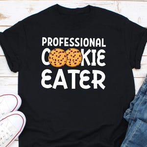 May include: Black t-shirt with white text that reads "Professional Cookie Eater" and a graphic of two chocolate chip cookies.