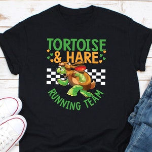 May include: Black t-shirt with a cartoon graphic of a turtle dressed as a rabbit, with the text "TORTOISE & HARE RUNNING TEAM". The design includes green and orange hearts and a checkered flag.