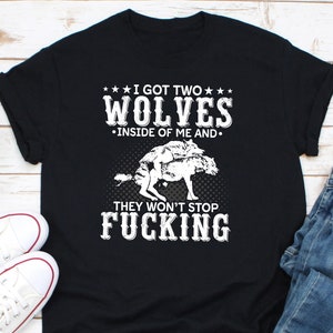 May include: Black t-shirt with white text and a graphic of two wolves. The text reads "I GOT TWO WOLVES INSIDE OF ME AND THEY WON'T STOP FUCKING."